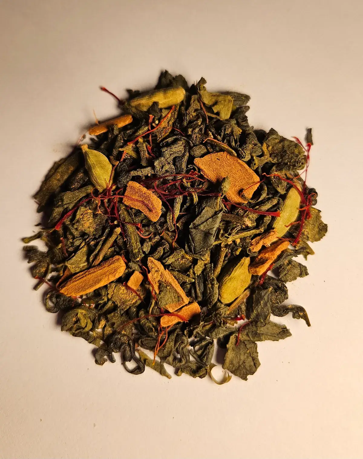 A close-up of the Velora loose-leaf blend: green tea leaves flecked with saffron threads, cinnamon bark and whole cardamom pods.